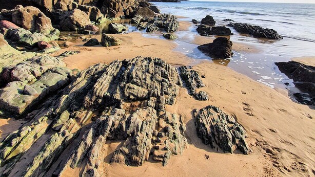 A rocky beach with clear water and a sandy shore.
