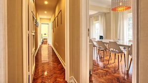 Un pasillo con piso de madera que conduce a un comedor con sillas blancas y una mesa.