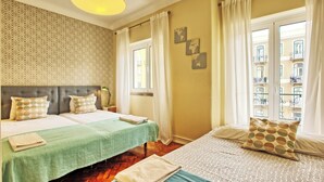 Habitación de hotel con dos camas, un papel tapiz estampado, vista de la ciudad a través de amplias ventanas y un globo decorativo colgante.