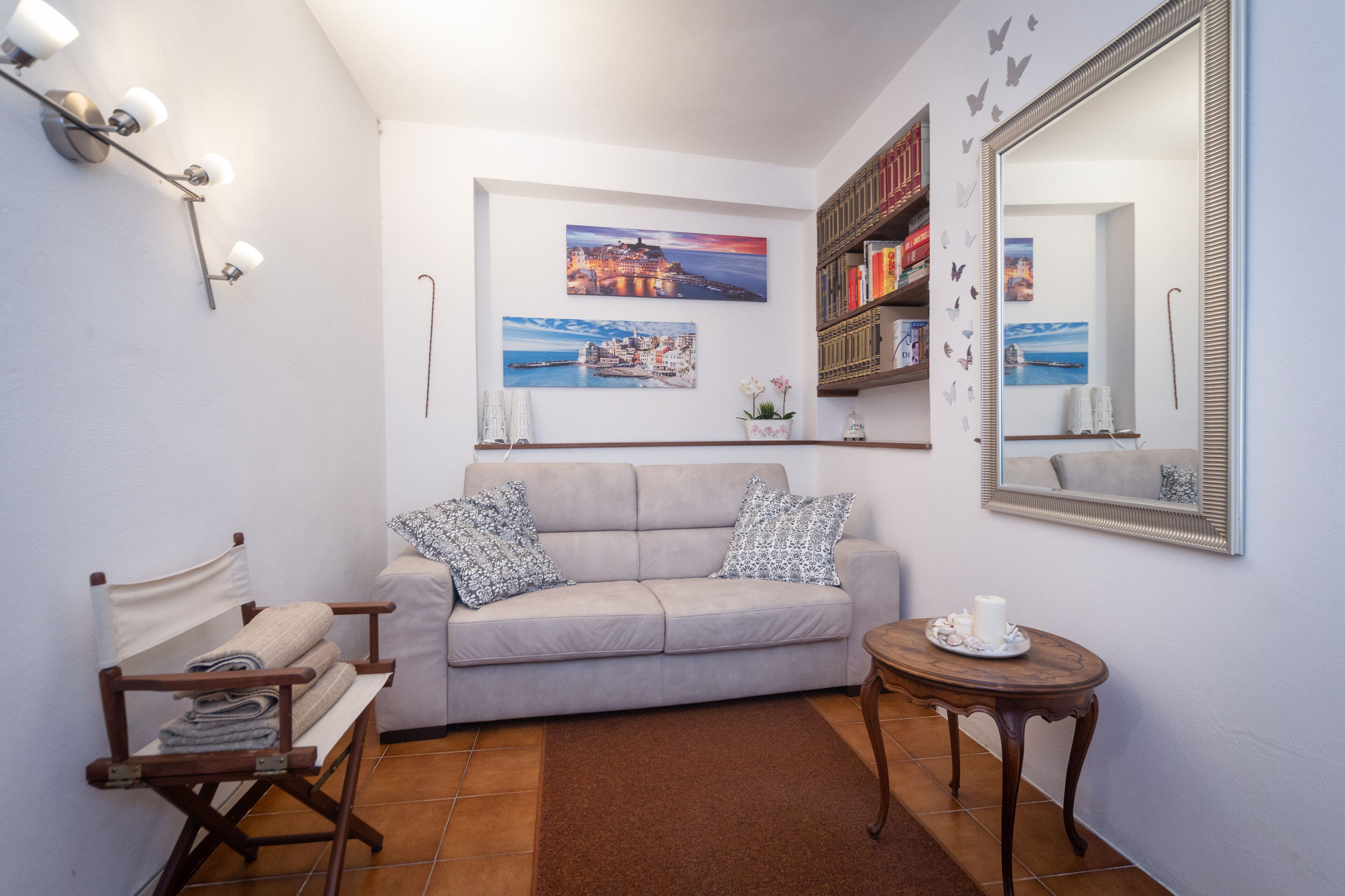 Un salon avec un canapé beige, une petite table sur laquelle est posée une bougie, une chaise de réalisateur et une bibliothèque.