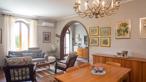 A spacious living room with a wooden dining table, comfortable seating, and a chandelier.