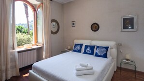 A bedroom with a large bed, a window with curtains, and a view of greenery outside.
