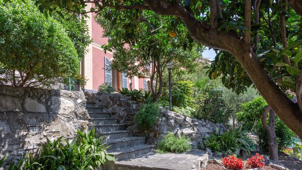 A stone staircase leading up to a building with a red facade, surrounded by lush greenery and a decorative bowl of red flowers.