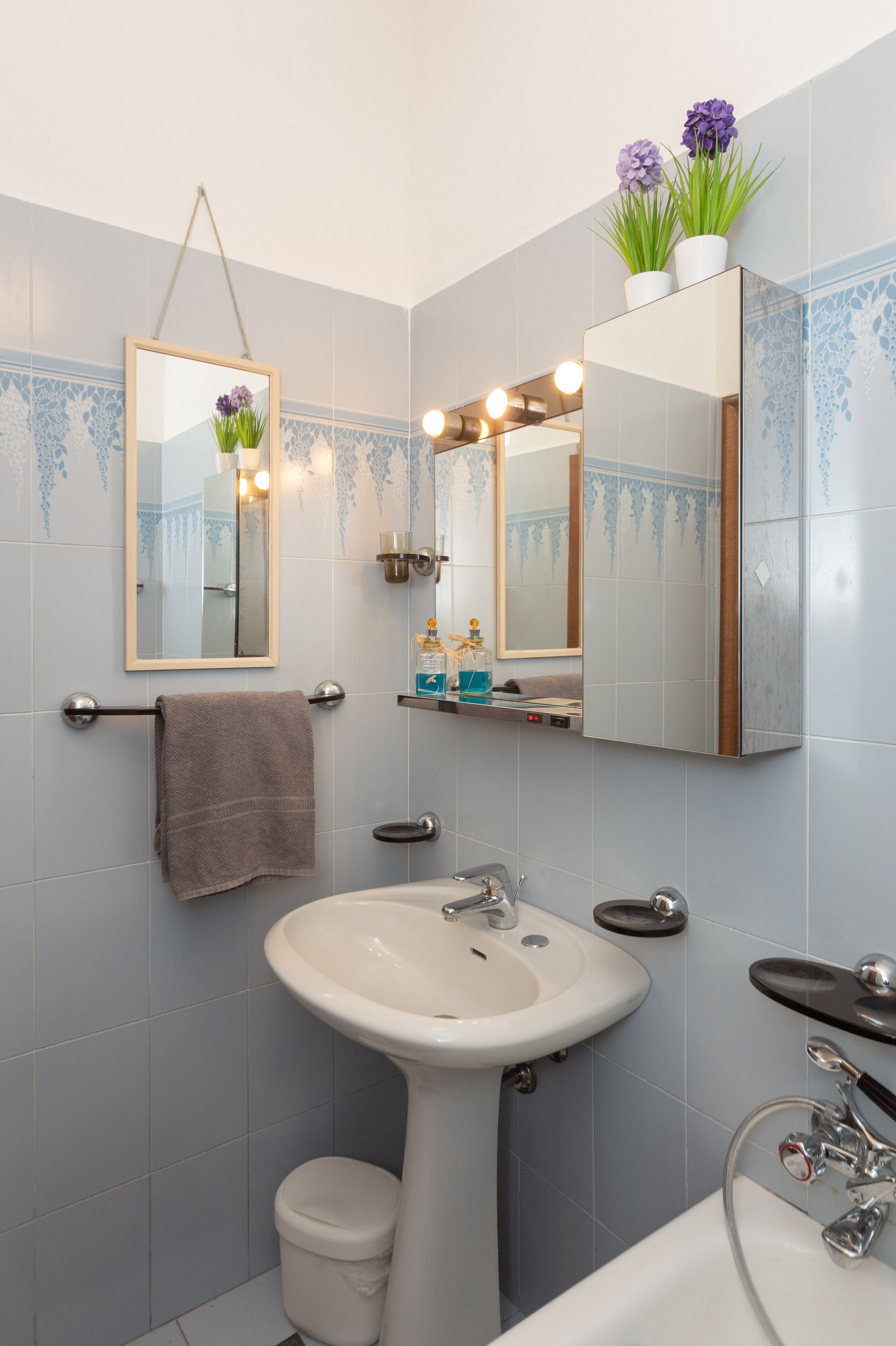 Un baño con lavamanos, inodoro y espejo. Hay plantas decorativas sobre el espejo y una toalla colgada en la pared.