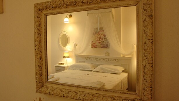 Ein Schlafzimmer mit einem großen, verzierten Spiegel, einer Nachttischlampe, einem Blumenbild und einem Himmelbett.