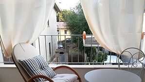 Ein Balkon mit einem Korbstuhl, einem Metalltisch und transparenten Vorhängen.