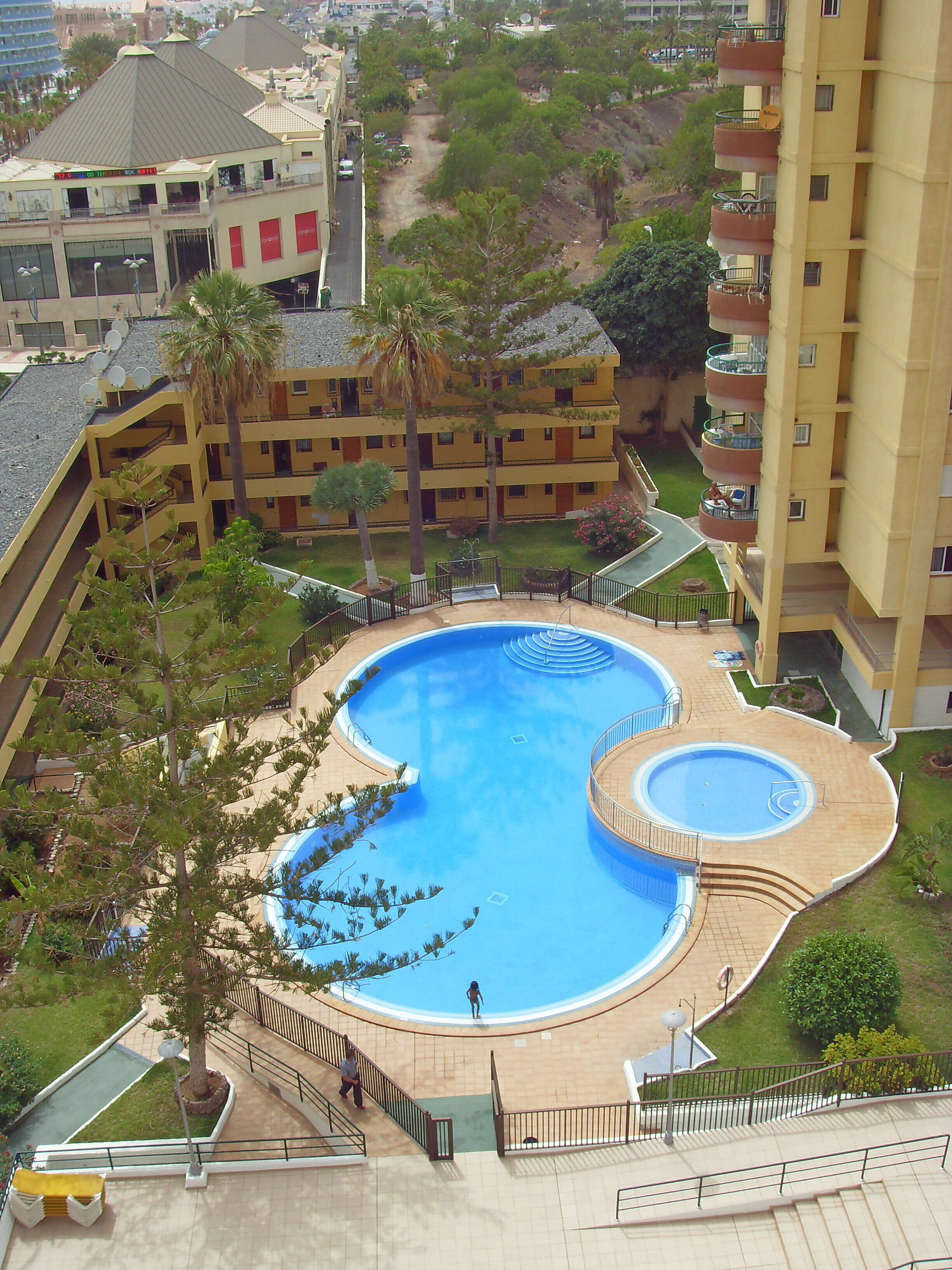 A multi-level hotel with a central swimming pool, outdoor terraces, and a landscaped garden.