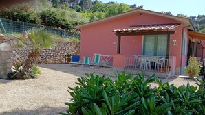 A small building with a tiled roof, a stone wall, and a gravel courtyard. There are two blue chairs and a table outside. - Villa Giuliana, small two-room apartment 3/4 Ptl. (Capoliveri (LI))