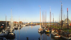 En småbåtshamn med många segelbåtar förtöjda, en klar himmel och en byggnad med ett rött tak i bakgrunden.