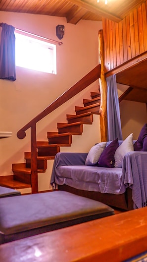 A room with a wooden staircase, a bed with a blue bedspread, and a window with curtains.