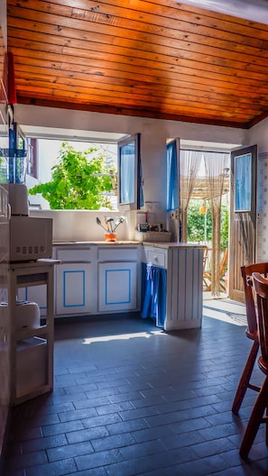 A kitchen with a wooden ceiling, a window with blue curtains, and a view of greenery outside.