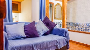 A room with a blue sofa, purple and white pillows, a wooden door, a mirror, and a tiled backsplash.