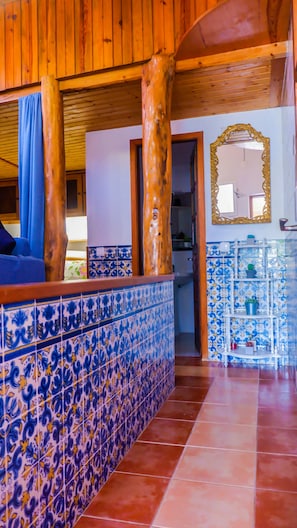 A room with a wooden ceiling, a tiled floor, and a bathroom with blue and white tiles.