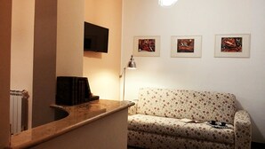 Una sala de estar con un sof á, un televisor montado en la pared y tres cuadros enmarcados.