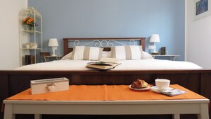 Una cama bien hecha con sábanas blancas, una mesita de noche con un libro y una taza, y una pequeña mesa con un croissant y una taza.