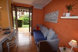 Quarto com cama, mesa de jantar com cadeiras, mesinha de cabeceira com abajur e um vaso de plantas.