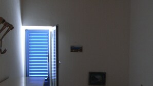 Une chambre avec un plafond en bois, un lit recouvert d’une couvre-lit à motifs, une petite fenêtre avec des stores et un tableau encadré accroché au mur.