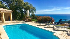 A swimming pool with stone tiles, a wooden table with chairs, and lounge chairs. - Villa with spectacular sea views and private pool in Begur (Begur)