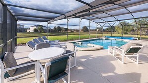 Un espacio al aire libre techado con piscina, sillas de descanso y una mesa.