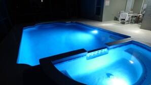 Una piscina con un borde iluminado en azul y una zona de hidromasaje.