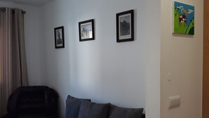 Un salon avec un canapé de couleur sombre, un fauteuil noir et trois tableaux encadrés accrochés au mur.