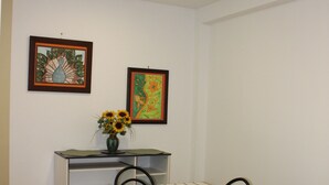 Un coin repas avec une table dressée pour quatre personnes, entourée de chaises dotées de coussins verts. Sur la table, on trouve un vase rempli de tournesols, et deux œuvres d’art encadrées ornent le mur.