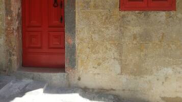 A red door with a metal grille and a red shutter on a weathered stone wall.