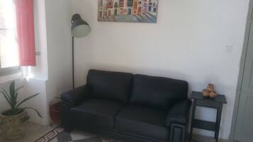 A room with a black sofa, a floor lamp, a potted plant, a small table with a vase, and a painting on the wall.