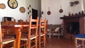 A dining area with wooden chairs and a table, a fireplace, and wall decorations including clocks and plates.