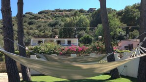 A hammock between trees in a grassy area with a view of houses and hills in the background.