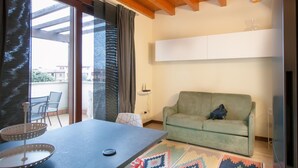 A modern living room with a sofa, a dining table with chairs, a patterned rug, and a large window with curtains. - Two bedroom apartment with pool view (Bassana)