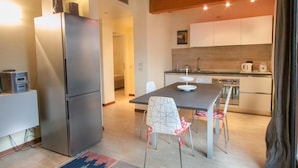 A modern kitchen with a built-in oven, a refrigerator, and a dining area with a table and chairs. - Two bedroom apartment with pool view (Bassana)