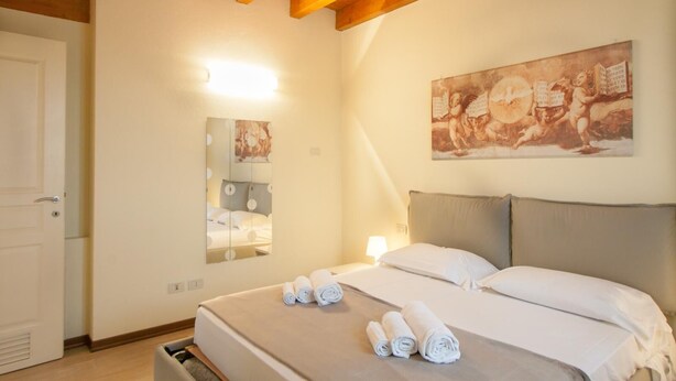 A hotel room with a bed, a mirror, a painting, and a door. - Two bedroom apartment with pool view (Bassana)
