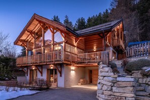 A wooden cabin with a balcony, stone wall, and a clear view of the surrounding forest. - Serre-Chevalier: 5-star luxury chalet, Spa area, panoramic view (La Salle-Les-Alpes)