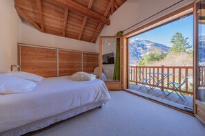 A bedroom with a wooden headboard, a bed with white linens, a green curtain, and a balcony with a wooden railing and tables. - Serre-Chevalier: 5-star luxury chalet, Spa area, panoramic view (La Salle-Les-Alpes)