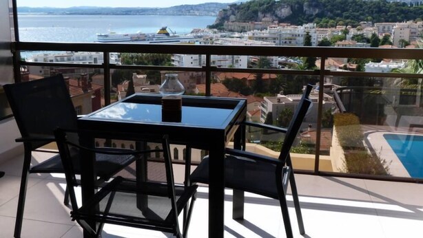 A balcony with a table and chairs, overlooking a body of water and a cityscape. - Superb modern apartment Panoramic sea view - Private garage (Nice)