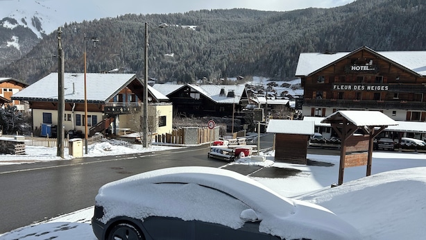 Een auto bedekt met sneeuw, geparkeerd voor een hotel met een bord waarop 'Fleur des Neiges' staat.
