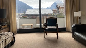 Een hotelkamer met een grote schuifglazen deur die leidt naar een balkon, een stoel, een bank, een televisie en een lamp.