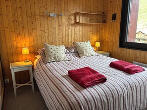 Une pièce aux murs lambrés, comprenant un lit, deux tables de chevet avec des lampes, une étagère au-dessus du lit et une fenêtre.