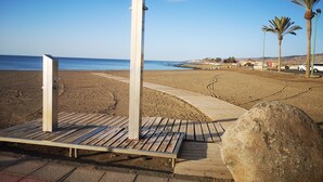 A beach with a wooden walkway, palm trees, and a large rock.