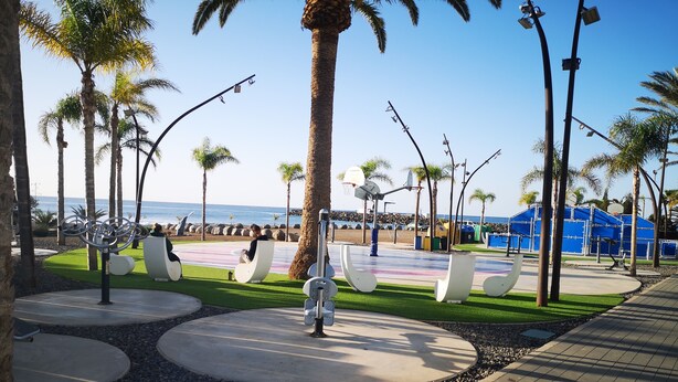 A park with modern seating, a basketball court, and a view of the sea.