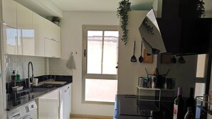 A modern kitchen with white cabinets, a Bosch washing machine, a black countertop, and a window providing natural light.