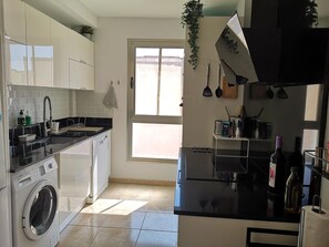 A modern kitchen with white cabinets, a Bosch washing machine, a black countertop, and a window providing natural light.