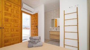 Quarto com cama, porta de madeira, ar condicionado, banheiro com espelho e porta-toalhas.