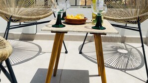 Uma varanda com cadeiras de vime, uma mesa, uma garrafa de bebida e uma tigela de petiscos.