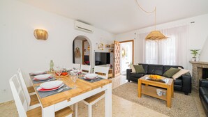 Uma sala de estar moderna com área de jantar, paredes brancas, lareira e televisão.