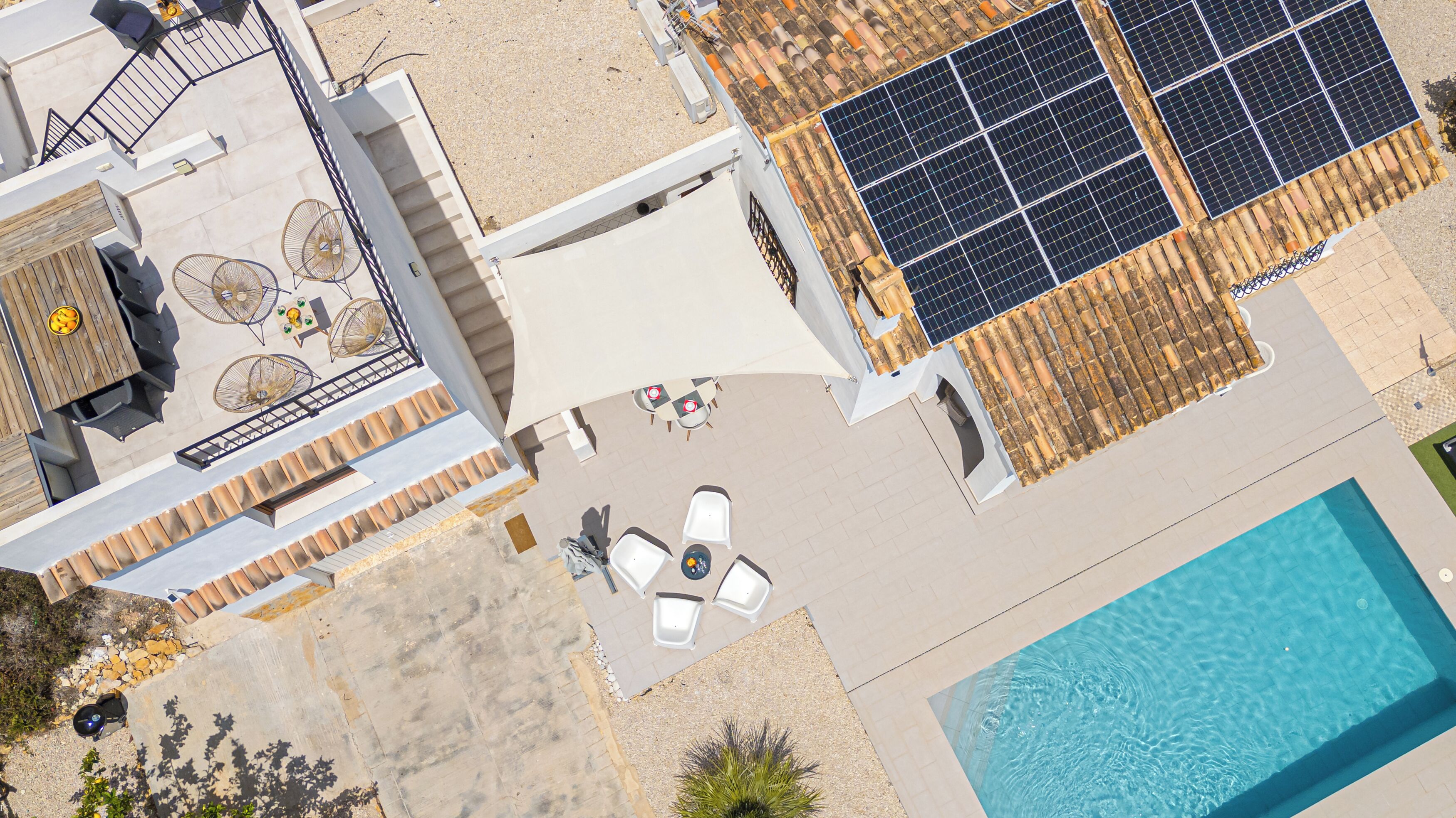 Ein Luftbild eines modernen Gebäudes mit Schwimmbad, Sitzbereich im Freien und Solaranlage.
