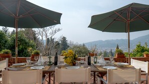 Un espace de restauration en plein air, avec des tables pour deux, entouré de plantes en pot et de parasols, offrant une vue panoramique sur les montagnes.