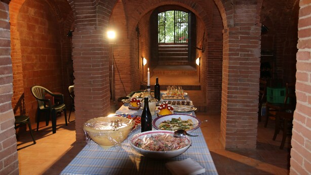Une pièce aux murs de briques, avec une table dressée pour un repas, comprenant divers plats et une bouteille de vin.