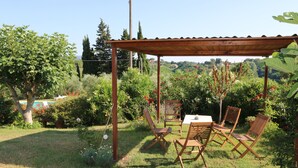 Une terrasse de jardin avec une table et des chaises, entourée d’une végétation luxuriante et offrant une vue sur la campagne.